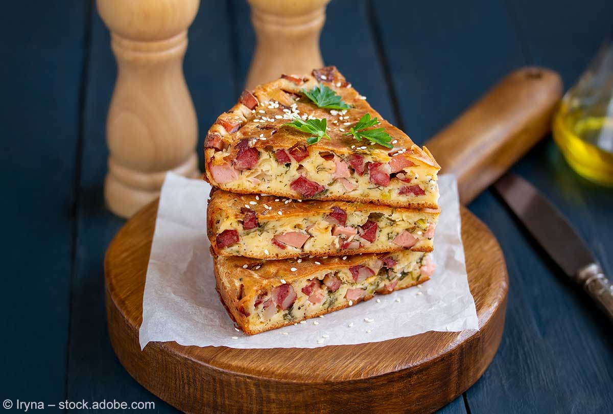 Drei übereinandergestapelte Stücke Egg and Bacon Pie auf einem Holzbrett