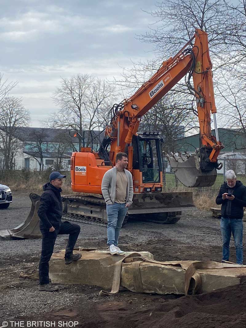 Robert Siebel (Mitte) mit zwei Mitarbeitern der Gartenbaufirma Peter Berg Gartendesign, die vor einem Bagger und auf großen Findlings-Steinen stehen