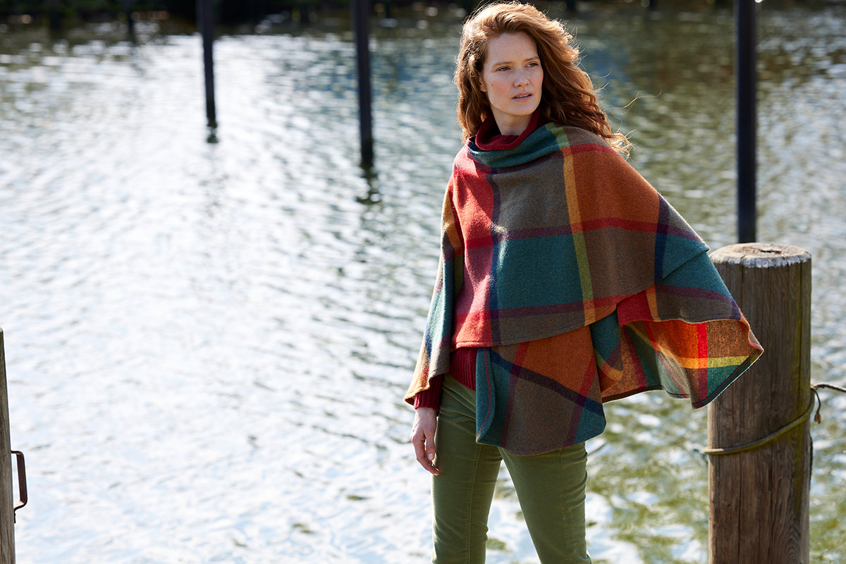 Herbstmode: Diese Stoffe halten Sie jetzt stilvoll warm Eine Frau am See, die ein Wollcape trägt.